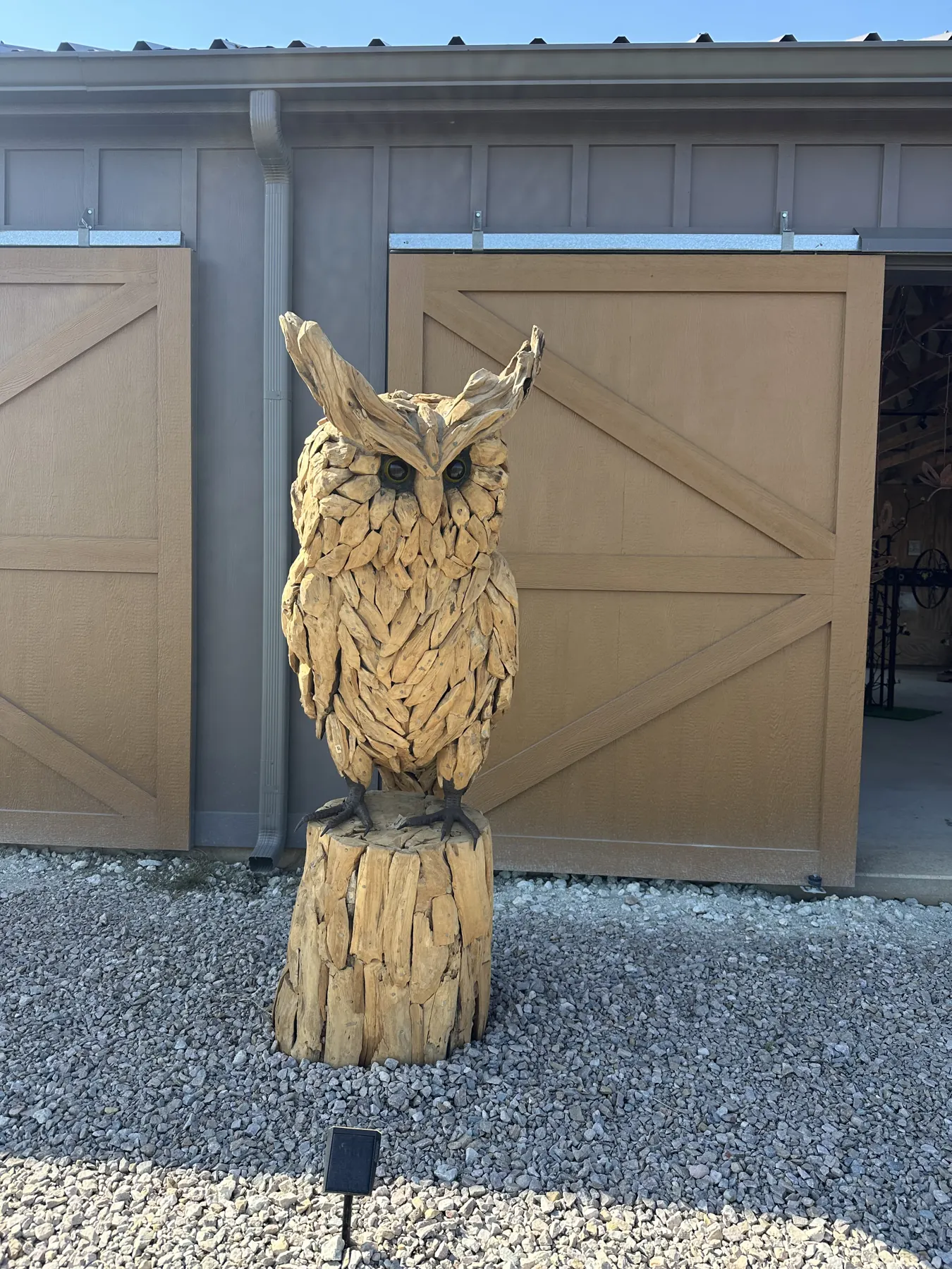 Hand-carved wooden owl sculpture standing in front of barn doors